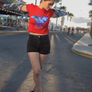 A woman playfully spinning with open arms on a sunny day, dressed in the Beauty in Bloom Tee in red, with the bold butterfly and rose artwork shining under the sunlight.