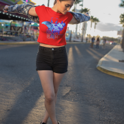 A woman playfully spinning with open arms on a sunny day, dressed in the Beauty in Bloom Tee in red, with the bold butterfly and rose artwork shining under the sunlight.