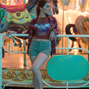 A woman leaning gracefully on a carousel railing, wearing the Beauty in Bloom Tee in coffee brown, capturing the whimsical charm of the butterfly and floral design.