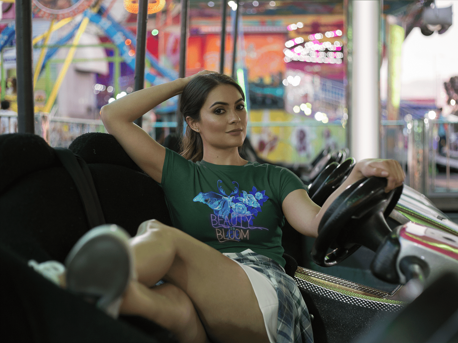 A woman relaxing in a bumper car at an amusement park, dressed in the Beauty in Bloom Tee in bottle green, showcasing the intricate butterfly and floral design.