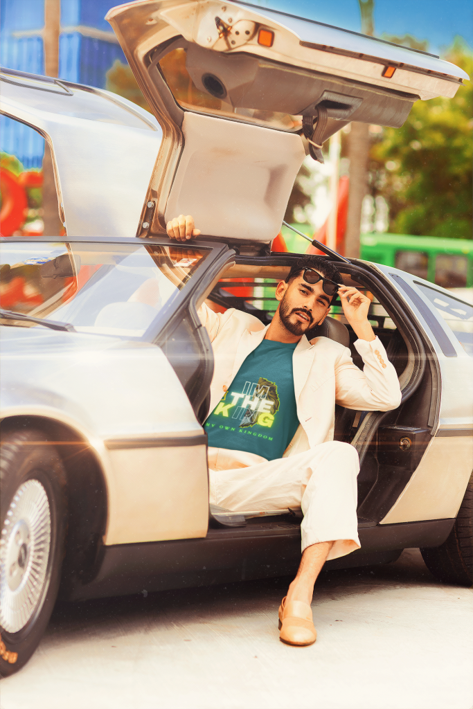 A relaxed man seated in a luxury car, wearing the "I'm the King Graphic Tee" in a vibrant teal shade. The bold lion-inspired design and his sunglasses add a touch of effortless charisma.