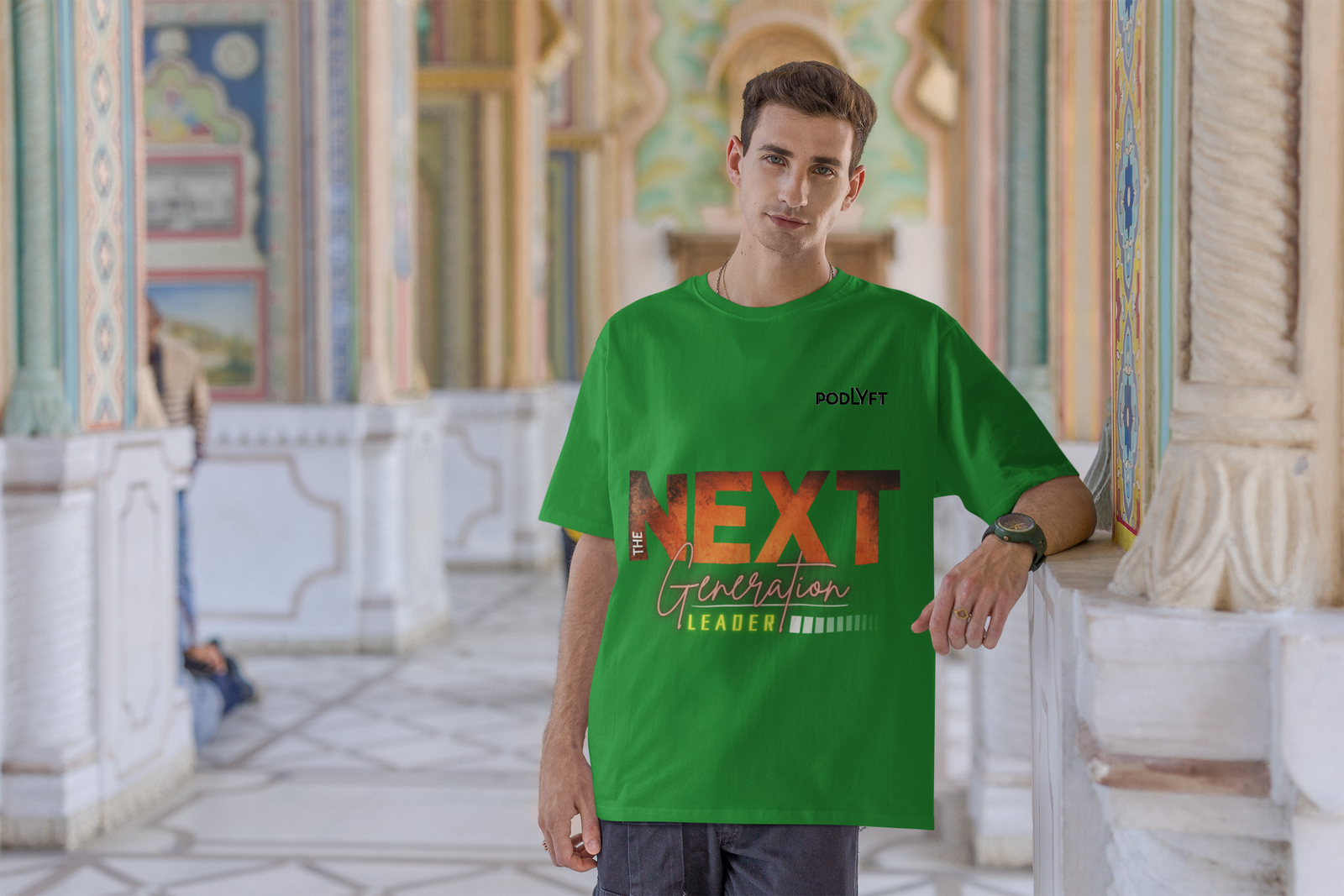 A fashionable young man wearing the Bold Next Generation Leader tee in green by PodLyft. The t-shirt’s striking design features a bold leadership statement with textured typography and vibrant highlights. The background features a grand, artistic interior, adding a touch of culture and sophistication to the visionary theme of the tee.
