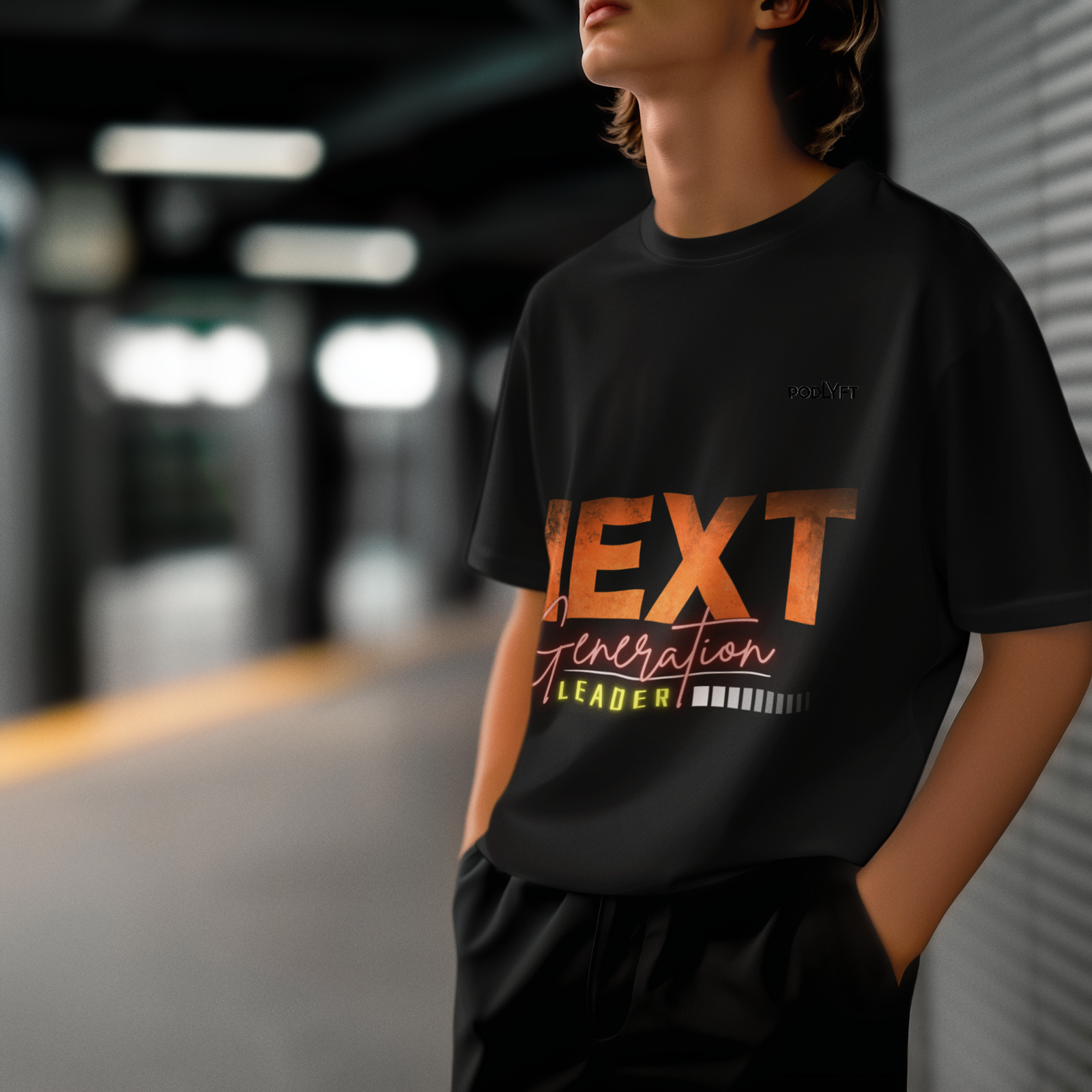 A modern and stylish young man wearing the Bold Next Generation Leader tee in black by PodLyft. The t-shirt showcases a dynamic leadership message with bold typography and a vibrant glow effect. The dark aesthetic and urban setting create a sleek, contemporary look, making this an ideal choice for confident changemakers."