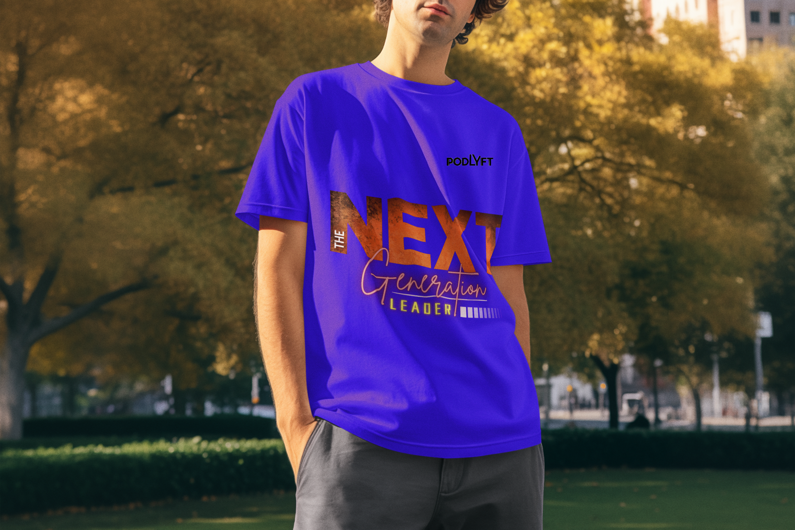 A stylish young man wearing the Bold Next Generation Leader tee in royal blue by PodLyft. The t-shirt features a striking leadership statement with 'NEXT' in textured orange, 'Generation' in elegant script, and 'LEADER' highlighted in a neon glow. The model stands confidently in an outdoor setting with golden autumn leaves in the background, exuding a bold and visionary vibe.