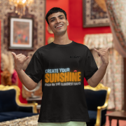 Motivational black oversized T-shirt with a bold 'CREATE YOUR SUNSHINE EVEN ON THE CLOUDIEST DAYS' design. Vibrant sky-blue, orange/yellow, and white text with a sun icon. DTG-printed on durable 240 GSM cotton fabric. Small size.