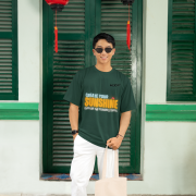 Bottle green oversized tee with a bright and uplifting 'CREATE YOUR SUNSHINE EVEN ON THE CLOUDIEST DAYS' design. Features sky-blue, orange/yellow, and white text with a sun icon. DTG-printed on soft 240 GSM cotton fabric. Medium size.