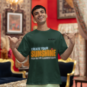 Motivational bottle green oversized T-shirt with a bold 'CREATE YOUR SUNSHINE EVEN ON THE CLOUDIEST DAYS' design. Vibrant sky-blue, orange/yellow, and white text with a sun icon. DTG-printed on durable 240 GSM cotton fabric. Small size.