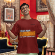 Motivational maroon oversized T-shirt with a bold 'CREATE YOUR SUNSHINE EVEN ON THE CLOUDIEST DAYS' design. Vibrant sky-blue, orange/yellow, and white text with a sun icon. DTG-printed on durable 240 GSM cotton fabric. Small size.