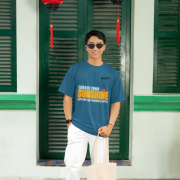 Petrol blue oversized tee with a bright and uplifting 'CREATE YOUR SUNSHINE EVEN ON THE CLOUDIEST DAYS' design. Features sky-blue, orange/yellow, and white text with a sun icon. DTG-printed on soft 240 GSM cotton fabric. Medium size.