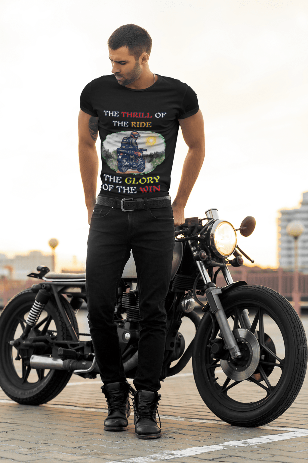 A stylish biker wearing the Thrill Rider Tee by PodLyft, standing confidently next to a classic black motorcycle. The black t-shirt features a bold design of a fearless motorcyclist riding through a scenic outdoor backdrop with a bright sun, green landscapes, and a winding road. The typography highlights "THE THRILL OF THE RIDE" and "THE GLORY OF THE WIN" in bold mixed colors, capturing the essence of adventure and freedom. A perfect tee for motorcycle enthusiasts, road warriors, and thrill-seekers who embrace the open road with passion and style.