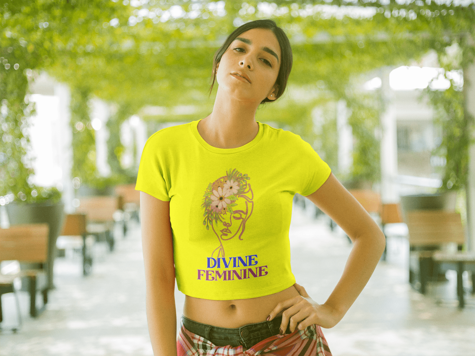 Woman wearing a vibrant yellow Divine Feminine T-shirt featuring a floral line-art design, posing confidently in a lush outdoor setting. A stylish and empowering nature-inspired tee, available at PodLyft.