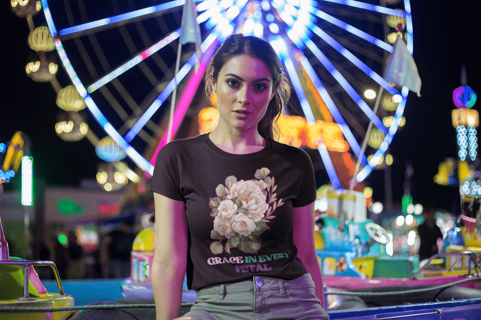 Grace in Every Petal Tee – A chic black floral t-shirt featuring a delicate white rose bouquet design, worn by a stylish model at a vibrant carnival with a glowing Ferris wheel in the background. A perfect blend of elegance and fun fashion.