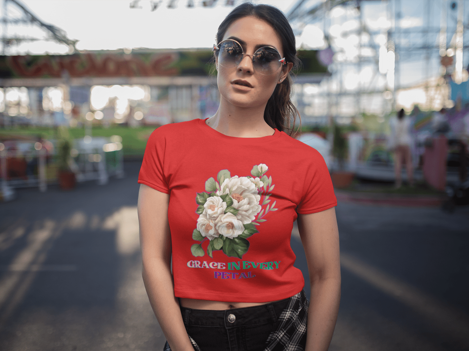 Grace in Every Petal Tee – A bold red floral crop top featuring a delicate white rose bouquet design, worn by a stylish model with sunglasses at an amusement park. A perfect combination of elegance and casual fashion.