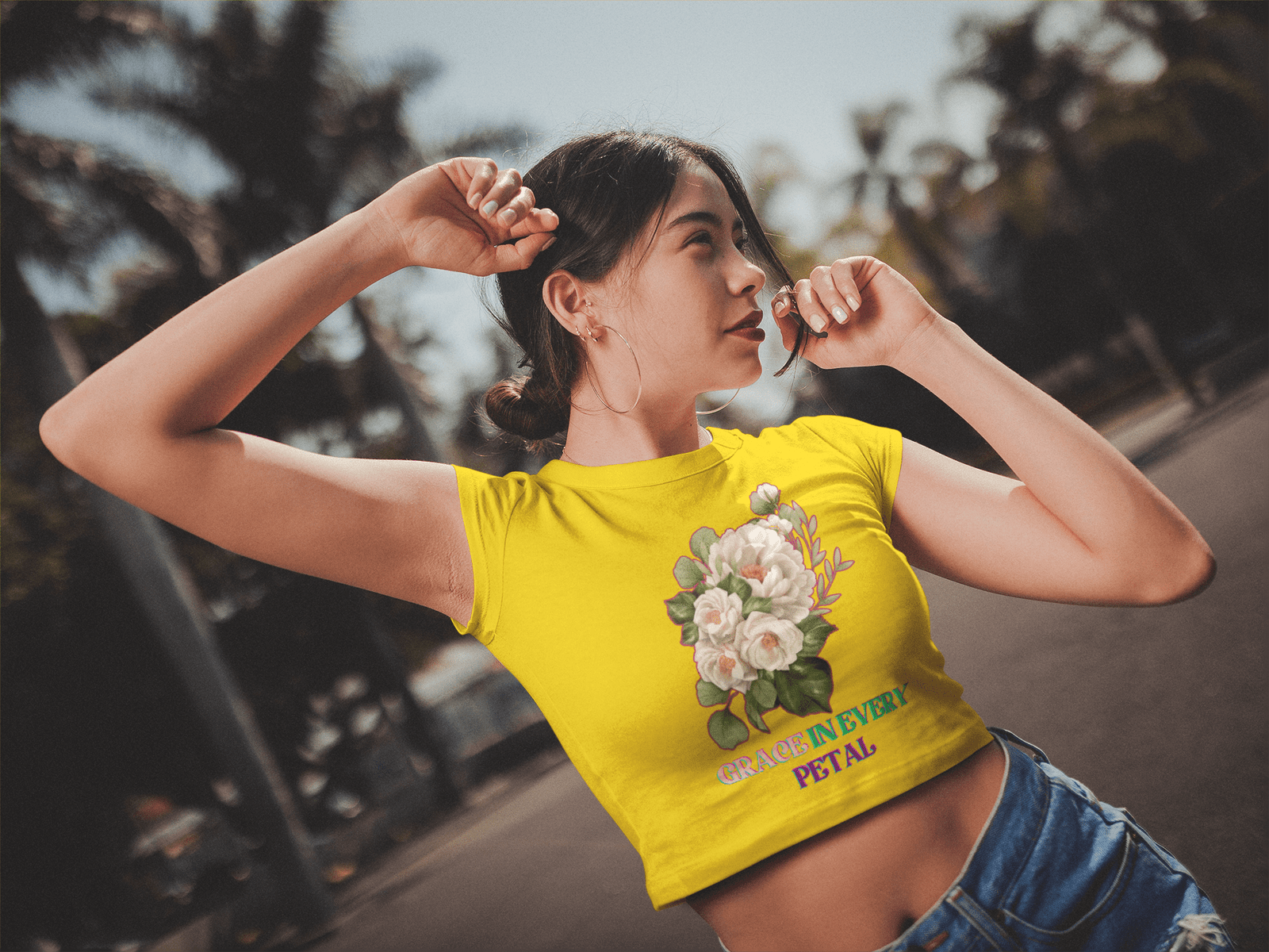 Grace in Every Petal Tee – A vibrant yellow floral crop top featuring an elegant white rose bouquet design, worn by a stylish model in a relaxed outdoor setting. A perfect blend of nature-inspired beauty and casual fashion.