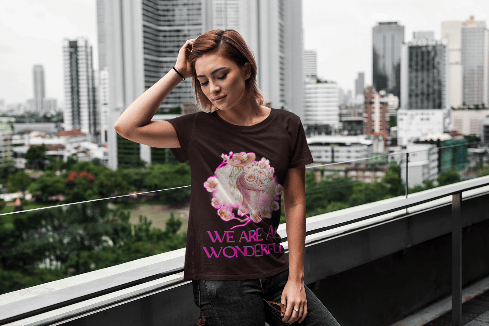 A trendy woman wearing the Coffee Brown 'Inspirational Floral Tee - We Are All Wonderful' by PodLyft, featuring a feminine floral design with a woman in a hat surrounded by pink flowers. A perfect blend of inspiration and fashion.