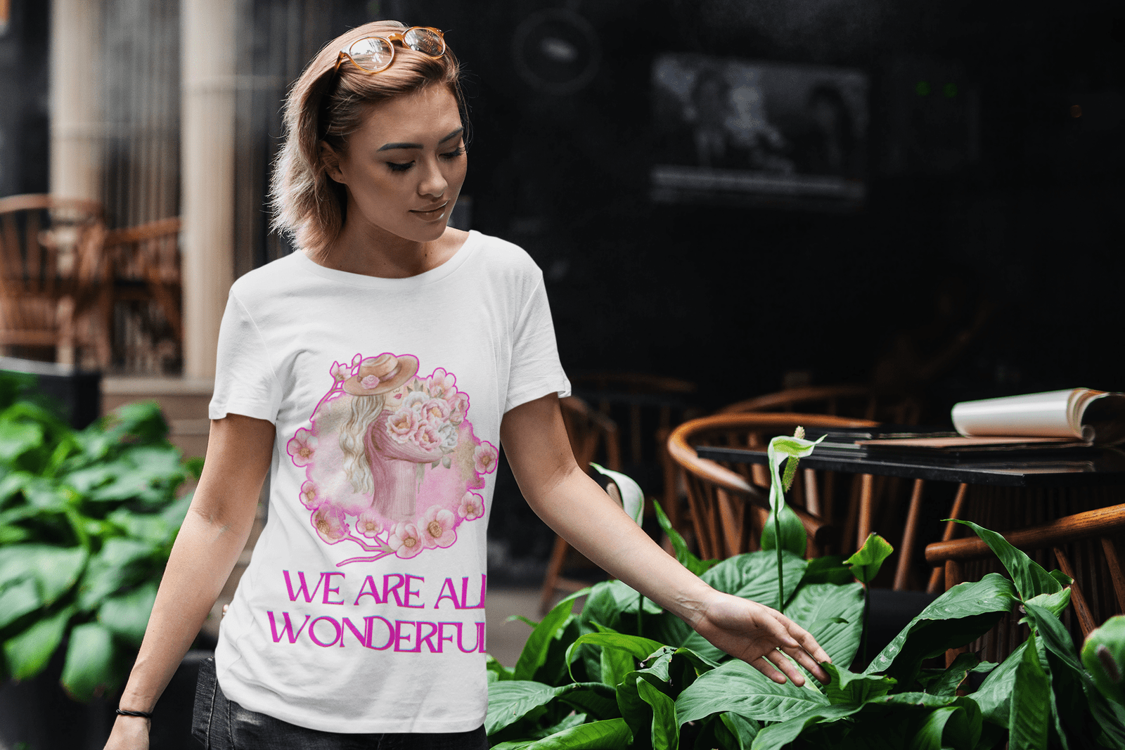 A stylish woman wearing the White 'Inspirational Floral Tee - We Are All Wonderful' by PodLyft, featuring a delicate floral and feminine design. A soft, uplifting fashion statement that celebrates beauty and confidence.
