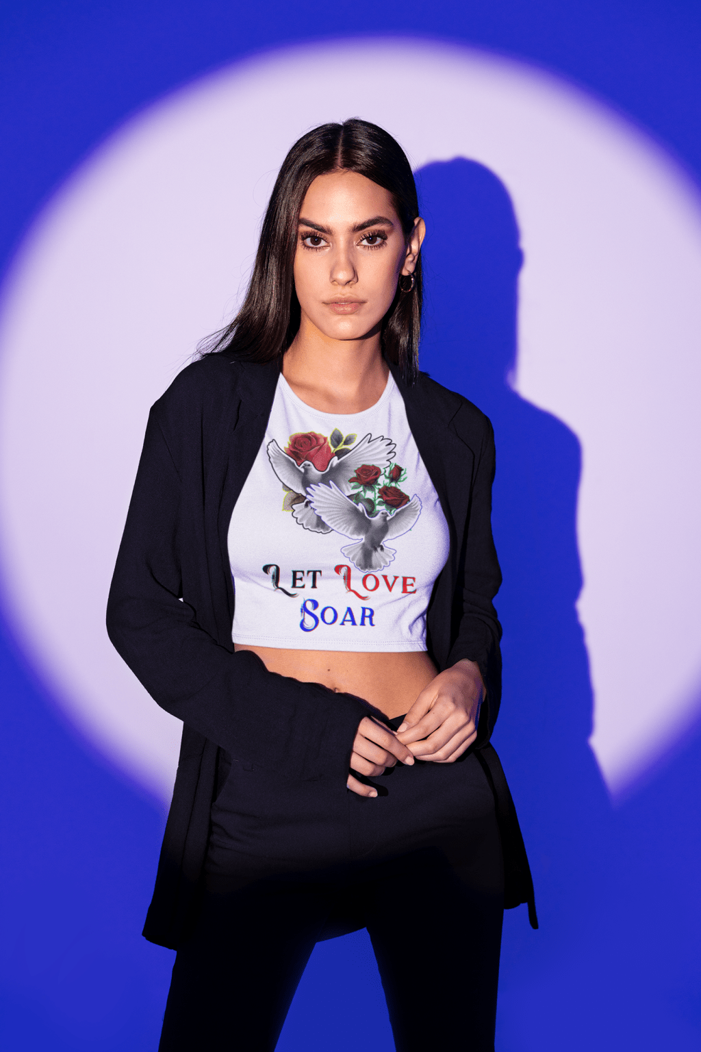 A stylish white Let Love Soar Tee featuring an elegant design of two doves carrying roses with the text "Let Love Soar" in a mix of red, black, and blue fonts. Perfect for expressing love, freedom, and passion. Modeled with a chic black blazer for a bold yet romantic look. High-quality apparel by PodLyft.
