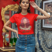 Model in a red 'Beauty with Innocence' crop top by PodLyft, showcasing a red-haired character with floral details and pink-green text, styled with light blue pants, posed against a tranquil sunset with mountains and a calm ocean in the distance.