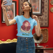 Model showcasing a sky blue 'Beauty with Innocence' crop top by PodLyft, with a red-haired character design, white flowers, and pink-green text, wearing light blue trousers, posed against a tranquil sunset with mountains and water in the distance.