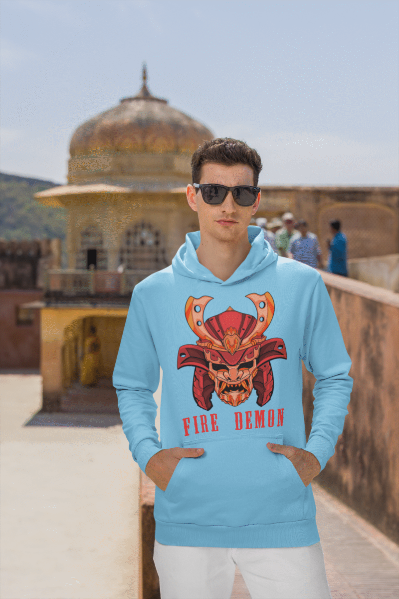 Men’s Fire Demon Samurai Hoodie by PodLyft in baby blue, on a mannequin, featuring a bold red and orange samurai helmet design with a demonic face and 'FIRE DEMON' text, displayed in a modern store with blurred clothing racks in the background.