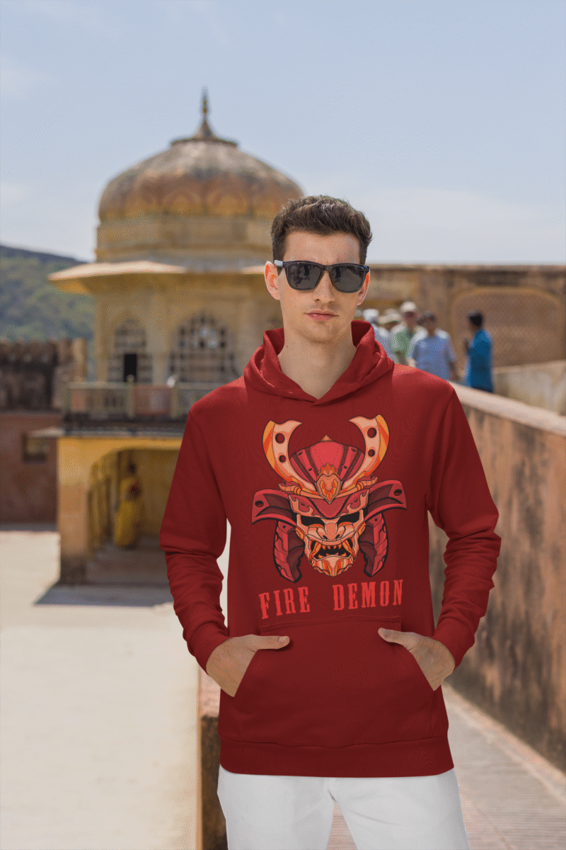 Men’s Fire Demon Samurai Hoodie by PodLyft in maroon, on a mannequin, featuring a bold red and orange samurai helmet design with a demonic face and 'FIRE DEMON' text, displayed in a modern store with blurred clothing racks in the background.
