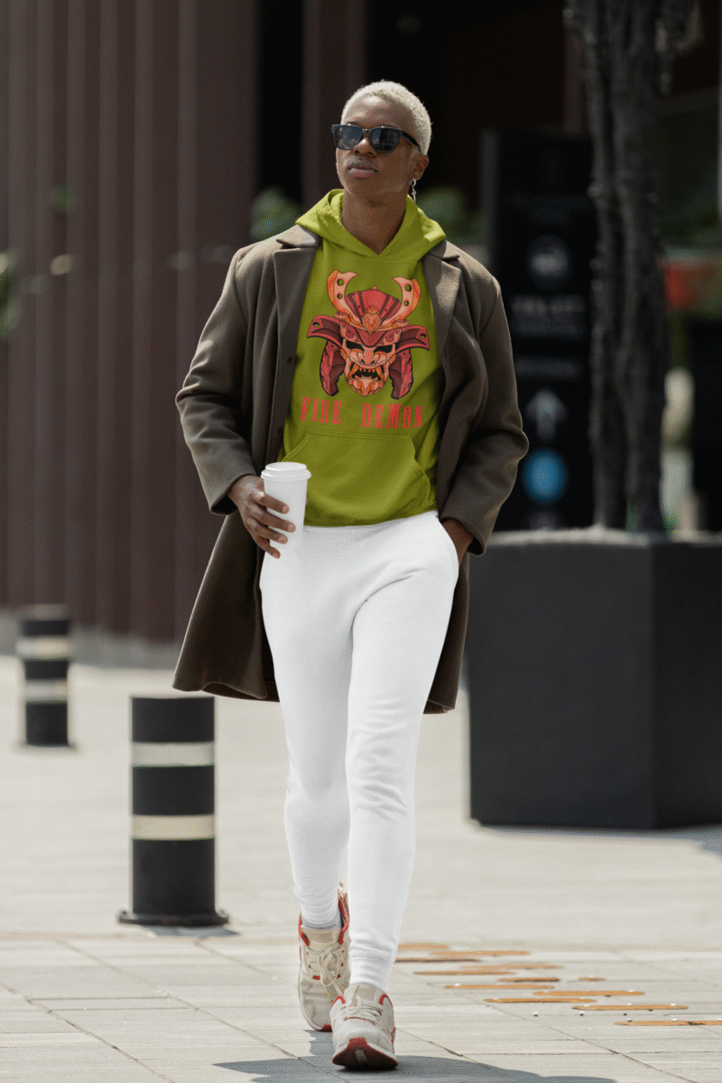 Men’s Fire Demon Samurai Hoodie by PodLyft in olive green, on a mannequin, featuring a bold red and orange samurai helmet design with a demonic face and 'FIRE DEMON' text, displayed in a modern store with blurred clothing racks in the background.