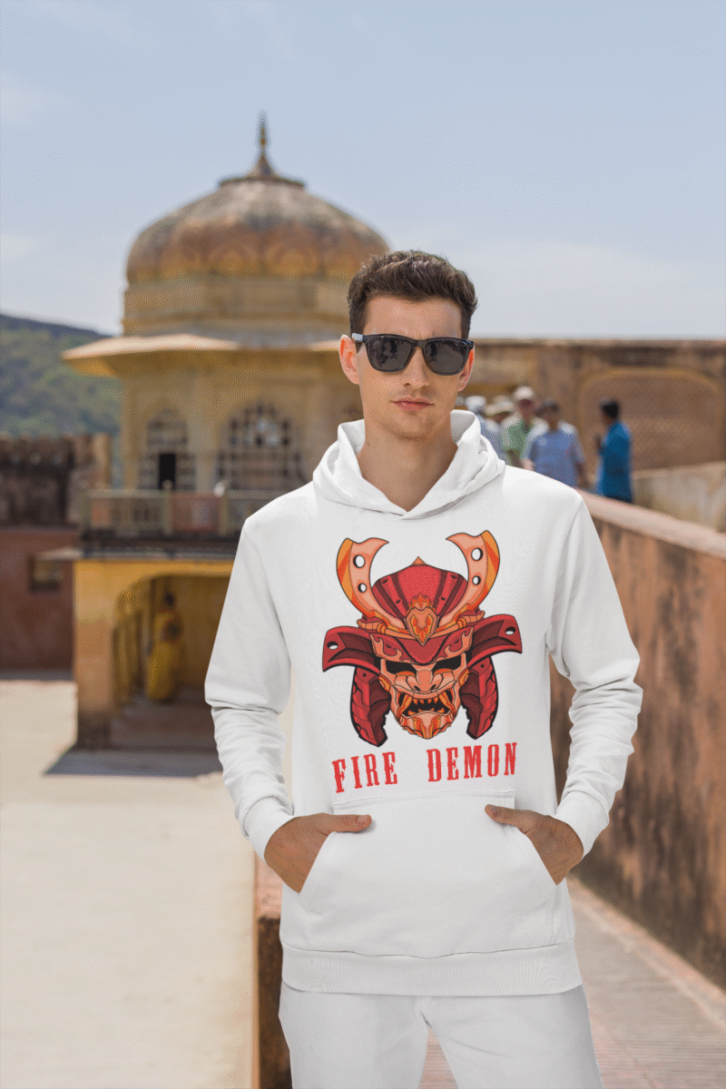 Men’s Fire Demon Samurai Hoodie by PodLyft in white, on a mannequin, featuring a bold red and orange samurai helmet design with a demonic face and 'FIRE DEMON' text, displayed in a modern store with blurred clothing racks in the background.