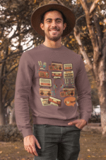 Man wearing a brown 90s retro sweatshirt featuring vintage cassette tapes, boomboxes, radios, and music icons, standing outdoors with a cheerful smile and autumn trees in the background — PodLyft retro sweatshirt for men.