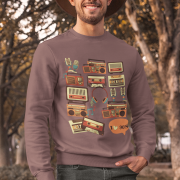 Man wearing a brown 90s retro sweatshirt featuring vintage cassette tapes, boomboxes, radios, and music icons, standing outdoors with a cheerful smile and autumn trees in the background — PodLyft retro sweatshirt for men.