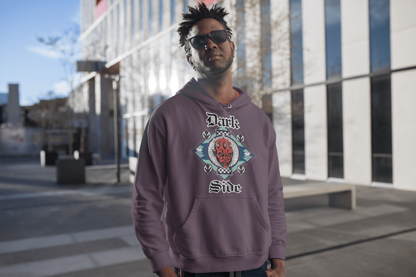 Model in a brown 'Official Darth Maul Hoodie' by PodLyft, displaying a red-and-black Darth Maul design with yellow eyes, set in a teal and mint green diamond frame, with 'Dark' and 'Side' in gothic white text, walking in a lush garden with greenery and a modern building in the background.