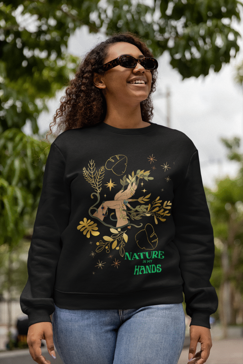 A black Nature in My Hands Sweatshirt with an eco-friendly design from PodLyft, featuring a DTG-printed graphic of hands holding nature elements like leaves and flowers on the front, displayed against a white background.