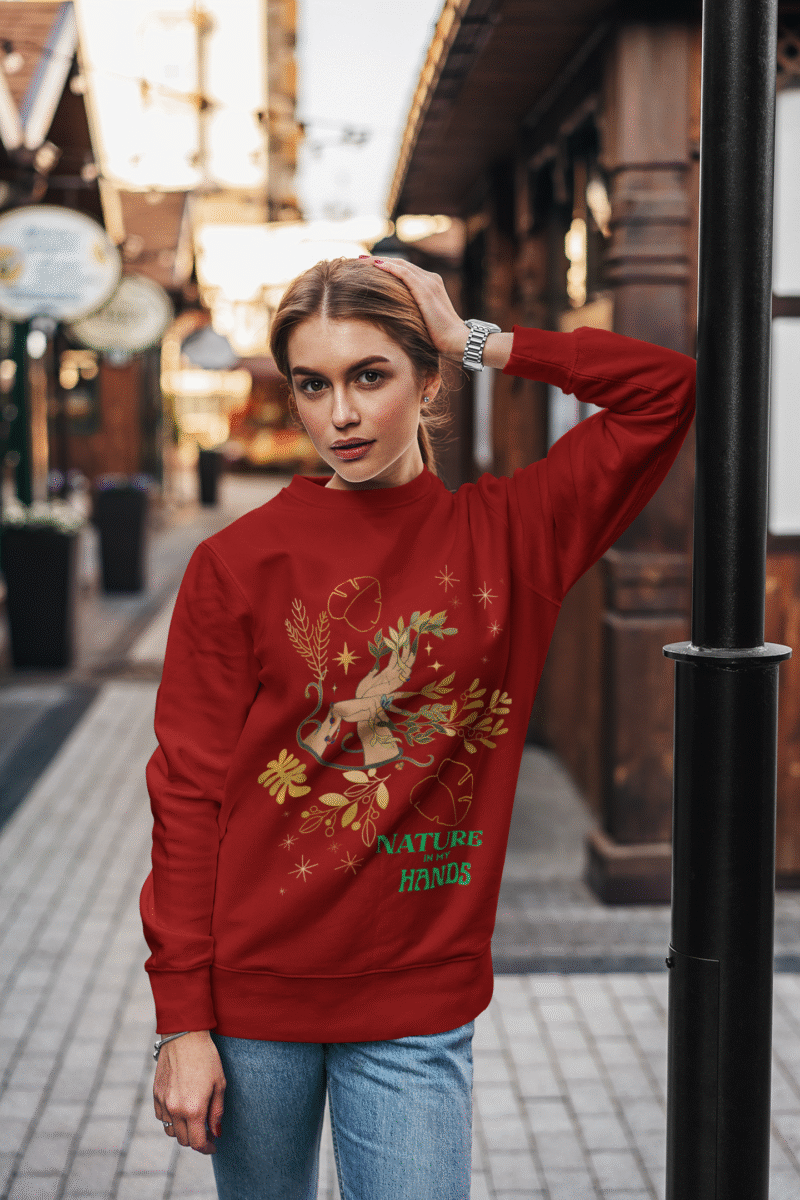 A maroon Nature in My Hands Sweatshirt with an eco-friendly design from PodLyft, showcasing a DTG-printed graphic of hands holding nature elements like leaves and flowers on the front, set against a white background.