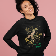 Smiling woman wearing the Nature in My Hands Sweatshirt, a black eco-friendly garment featuring a symbolic design of a hand intertwined with green and gold botanical elements, mystical stars, and the phrase "NATURE IN MY HANDS" in bold green text; posed against a soft pink background.