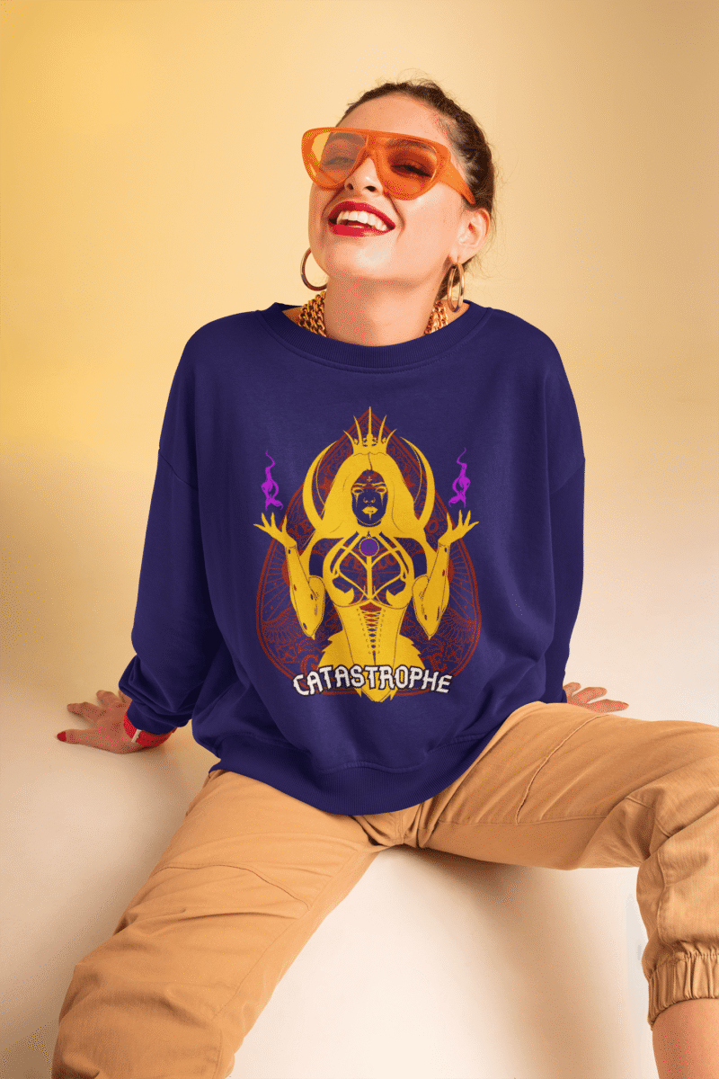 Woman wearing the PodLyft Women's Catastrophe Mystic Sweatshirt in deep purple, featuring a bold mystical enchantress design in gold and red with glowing purple flames, sitting against a soft beige background while smiling confidently.