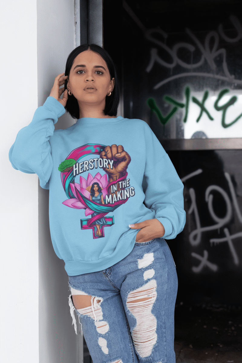 A woman wearing a navy blue PodLyft Feminist Power Sweatshirt, featuring a bold graphic with a female symbol, a lotus flower, a raised fist, and the text "HERSTORY IN THE MAKING," standing indoors.