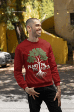 A smiling man wearing a maroon PodLyft Men's Plant the Future Sweatshirt, featuring a prominent tree design with roots and the text "PLANT THE FUTURE," posing outdoors with his hands in his pockets.