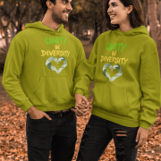 A man and a woman, possibly a couple, holding hands and looking at each other in an outdoor setting with autumn leaves on the ground and blurred trees in the background. They are both wearing olive green Unity in Diversity hoodies, which feature a graphic of hands of various skin tones forming a heart shape.