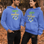 A man and a woman, possibly a couple, holding hands and smiling at each other in an outdoor setting with autumn leaves on the ground and blurred trees in the background. They are both wearing royal blue Unity in Diversity hoodies, which feature a graphic of hands of various skin tones forming a heart shape.