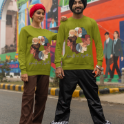A couple, possibly of South Asian descent, standing side-by-side in front of a colorful mural. The man, wearing a black turban, and the woman, wearing a red headscarf, are both wearing olive green Unity in Together sweatshirts. The sweatshirts feature a circular graphic with diverse profiles of people. The woman has her arm around the man's shoulder.