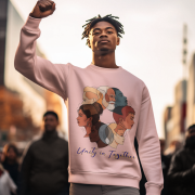 A young man, appearing to be of Black ethnicity, is pictured outdoors raising his fist in the air, wearing a light pink men's unity in together sweatshirt. The sweatshirt features a circular graphic displaying diverse faces of people from various backgrounds, with the text 'Unity in Together' beneath it. The setting appears to be a city street at dusk or dawn, with blurred figures in the background.