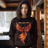 A young woman, possibly of Caucasian descent, with light brown hair pulled back, wearing a PodLyft Phoenix Reign sweatshirt. The sweatshirt features a graphic of a stylized, fiery phoenix with the text "I BURN I RISE I REIGN" below it. She is looking directly at the camera with a confident expression, standing against a plain light grey background.