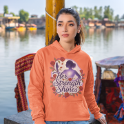 A young woman, possibly of East Asian descent, with dark hair, wearing a coral PodLyft women's empowered hoodie. The hoodie features an abstract graphic with geometric shapes and subtle lines in shades of purple and pink, conveying a message of empowerment. She is smiling confidently, with her hands in her pockets, standing against a blurred outdoor background.