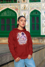 A young woman, possibly of East Asian descent, with dark hair, wearing a maroon PodLyft women's empowered hoodie. The hoodie features an abstract graphic with geometric shapes and subtle lines in shades of purple and pink, conveying a message of empowerment. She is looking directly at the camera with a confident expression, standing against a blurred grey background.