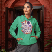 A young woman, possibly of East Asian descent, with dark hair, wearing a mint green PodLyft women's empowered hoodie. The hoodie features an abstract graphic with geometric shapes and subtle lines in shades of purple and pink, conveying a message of empowerment. She is smiling confidently, holding a small purple clutch bag, standing against a blurred outdoor background.