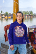 A young woman, possibly of East Asian descent, with dark hair, wearing a navy blue PodLyft women's empowered hoodie. The hoodie features an abstract graphic with geometric shapes and subtle lines in shades of purple and pink, conveying a message of empowerment. She is looking directly at the camera with a subtle smile, standing against a blurred grey background.
