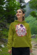 A young woman, possibly of East Asian descent, with dark hair, wearing an olive green PodLyft women's empowered hoodie. The hoodie features an abstract graphic with geometric shapes and subtle lines in shades of purple and pink, conveying a message of empowerment. She is smiling confidently, with her hands in her pockets, standing against a blurred outdoor background.