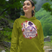 A young woman, possibly of East Asian descent, with dark hair, wearing an olive green PodLyft women's empowered hoodie. The hoodie features an abstract graphic with geometric shapes and subtle lines in shades of purple and pink, conveying a message of empowerment. She is smiling confidently, with her hands in her pockets, standing against a blurred outdoor background.