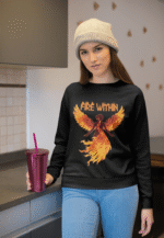 A young woman, possibly of Caucasian descent with light brown hair, wearing a black PodLyft women's Fire Within sweatshirt. The sweatshirt features a graphic of a human heart with stylized flames emanating from its top, and the text "FIRE WITHIN" written above and below it. She is looking directly at the camera with a subtle smile, standing against a plain light grey background.