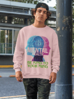 A young man, possibly of Caucasian descent, with short dark hair and a beard, wearing a baby pink PodLyft Mental Wellness Sweatshirt for men. The sweatshirt features a circular graphic with the letters "BKTYM" prominently in the center, surrounded by the phrase "BE KIND TO YOUR MIND." He is looking directly at the camera with a confident expression, standing against a plain light grey background.
