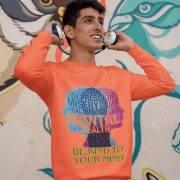 A young man, possibly of Caucasian descent, with short dark hair and a beard, wearing a coral PodLyft Mental Wellness Sweatshirt for men. The sweatshirt features a circular graphic with the letters "BKTYM" prominently in the center, surrounded by the phrase "BE KIND TO YOUR MIND." He is looking directly at the camera with a confident expression, standing against a plain light grey background.